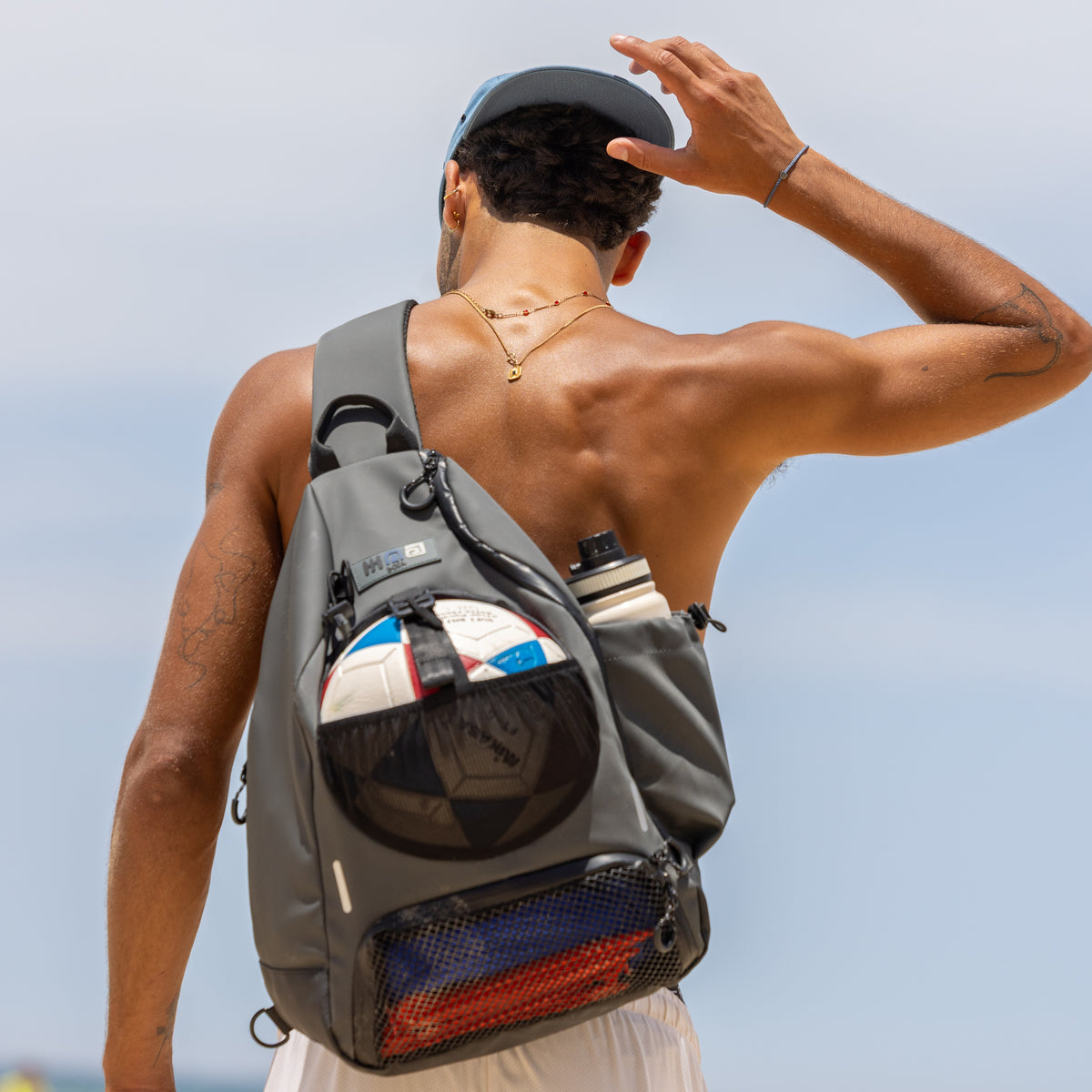 Person wearing a grey BORA crossbody sports bag carrying a ball and water bottle, viewed from behind